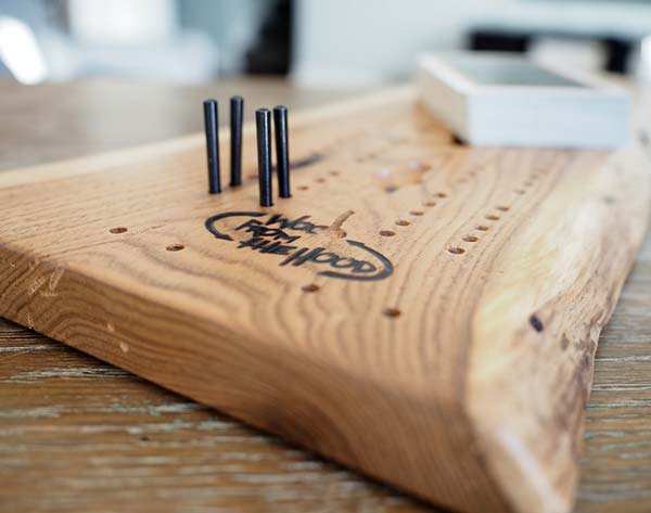 up close of a wooden cribbage board with black pegs and a boxed deck of cards