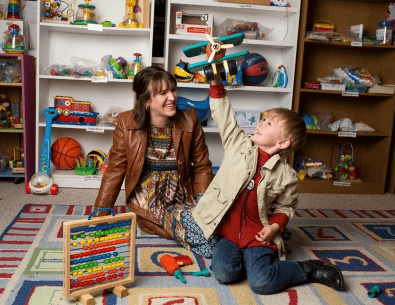 Boy playing with wooden plane toy while mom watches