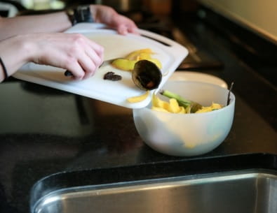 Close up of hands pushing organics scraps into bowl