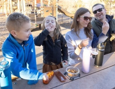 Family at a picnic table eating snacks from reusable containers