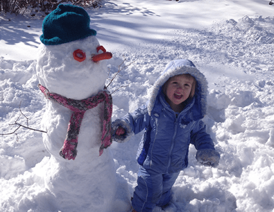 Young girl playing in snow with snowman