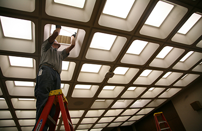 Person on a ladder changing an office light fixture