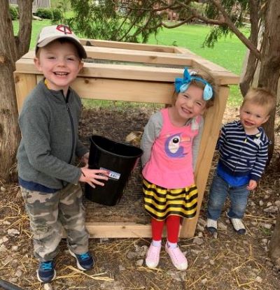 Three excited kids standing in front of a backyard compost bin