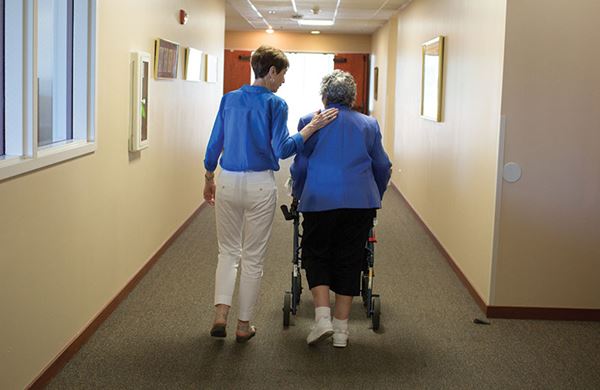 women walking a senior citizen down a hallways